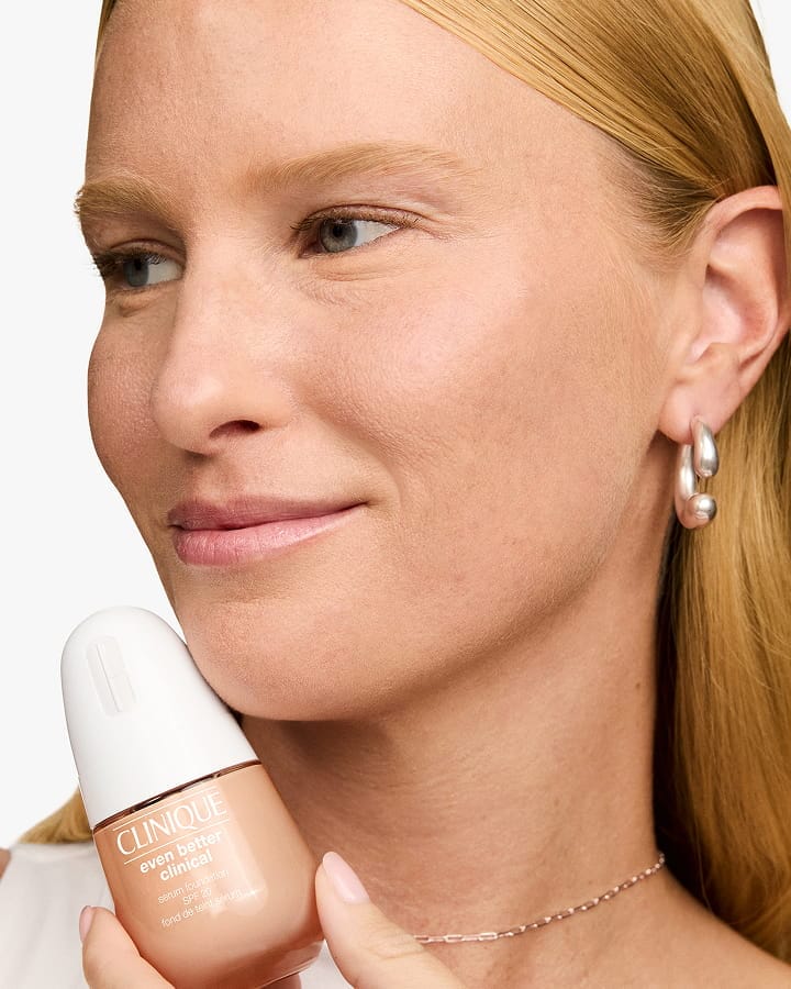 Close up of smiling, bearded man applying Clinique For Men Anti-Age Eye Cream to under eyes, in a bright setting