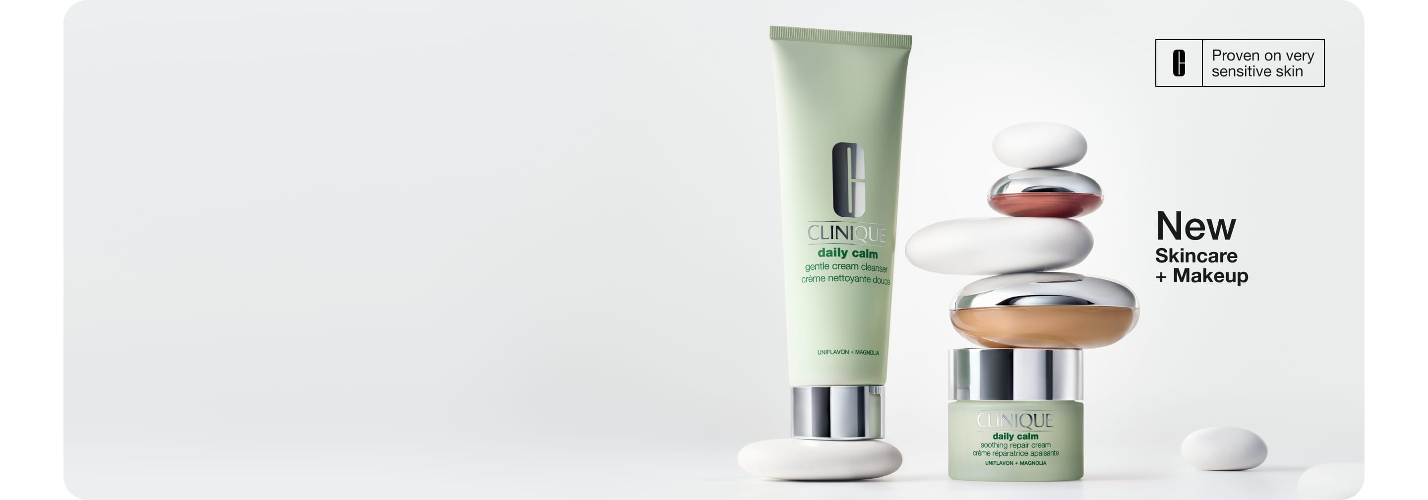 Model smilling applying product to face, next to New Clinique Daily Calm™ Collection dynamically placed on grey pebble stones